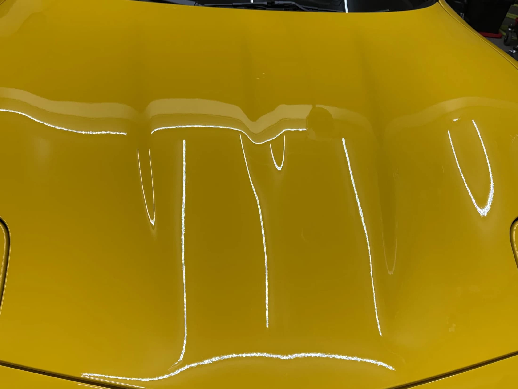 Glossy yellow hood with shop light reflections.